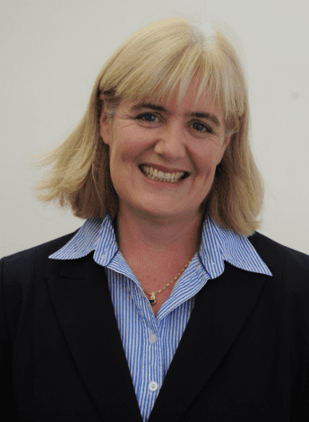 A woman with blonde shoulder-length hair is wearing a blue collared shirt. 